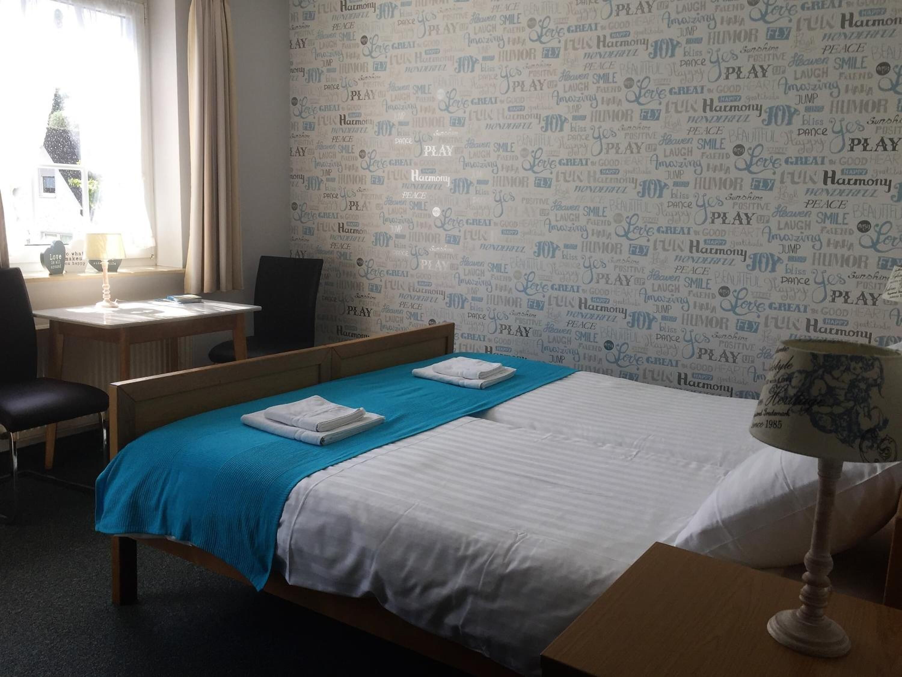 Habitación de hotel con cama, escritorio y silla. La habitación tiene una ventana con cortinas.