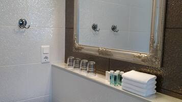 Une salle de bain avec un lavabo blanc, un miroir doté d’un cadre décoratif et une étagère contenant des articles de toilette.