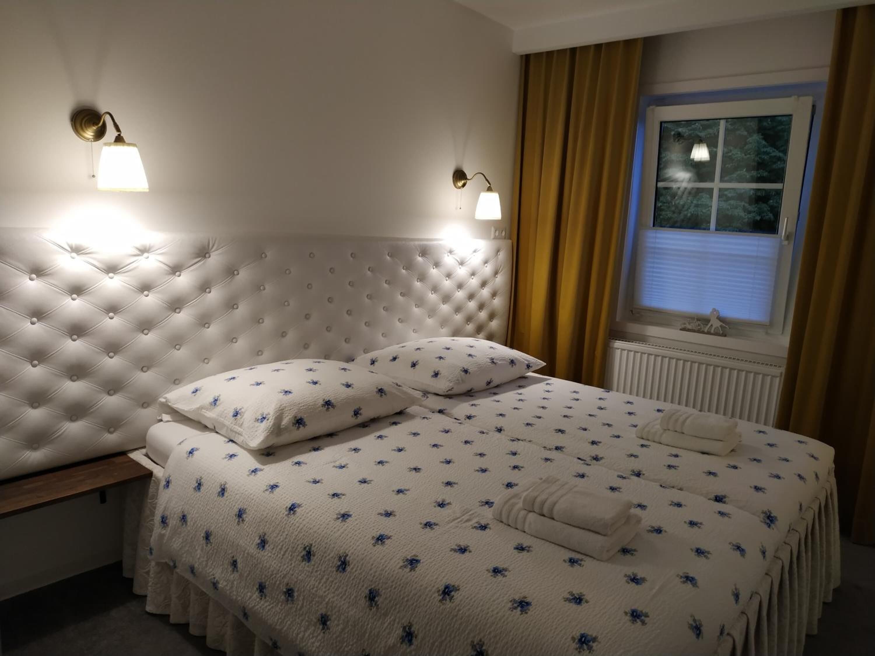 Un lit bien fait, avec une couette à motifs floraux, deux oreillers et une serviette pliée.