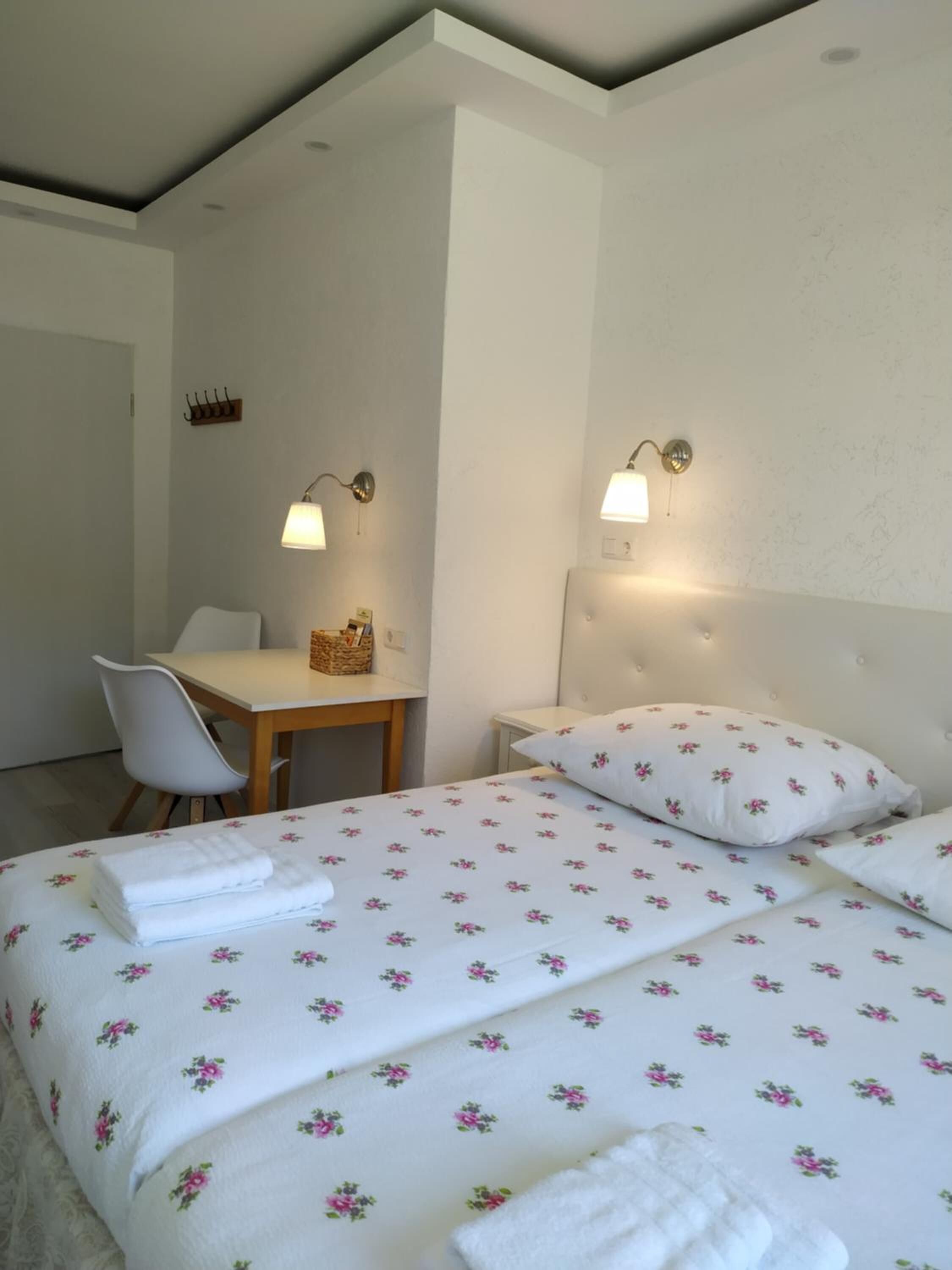 A hotel room with a bed, a desk, a chair, and two wall-mounted lamps.