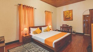 A hotel room with a wooden ceiling, a bed with an orange bedspread, two lamps, a zebra-patterned rug, a painting on the wall, and a wooden door. - Avian Breeze (Nuwara Eliya)