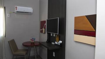 Quarto pequeno com escrivaninha, cadeira, ar condicionado, TV de tela plana e obras de arte na parede.