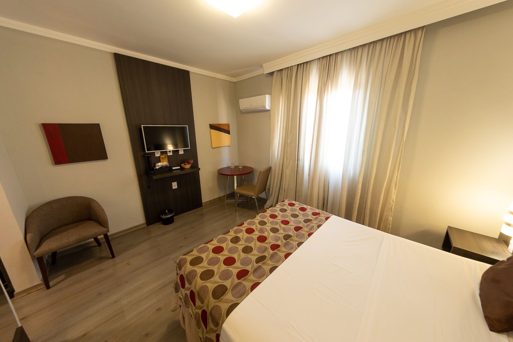 Habitación de hotel con cama, televisión, escritorio, silla y ventana con cortinas.