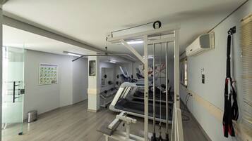 Une salle de sport équipée de matériel d’exercice, une affiche accrochée au mur et une poubelle.