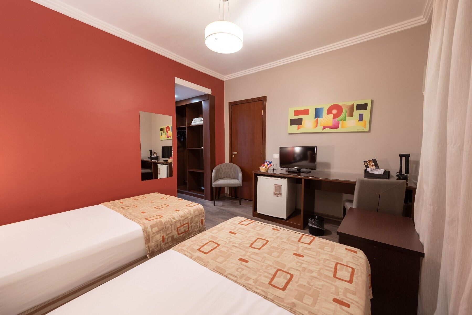 A hotel room with two beds, a desk with a television, a chair, and a wardrobe.