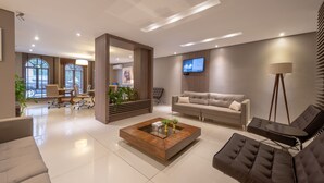 A modern living room with a sofa, a coffee table, and a TV mounted on the wall. - Class Hotel Guaxupé (Guaxupé)