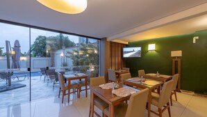 A modern dining area with glass walls, wooden tables, and chairs, featuring a view of the outdoors. - Class Hotel Guaxupé (Guaxupé)