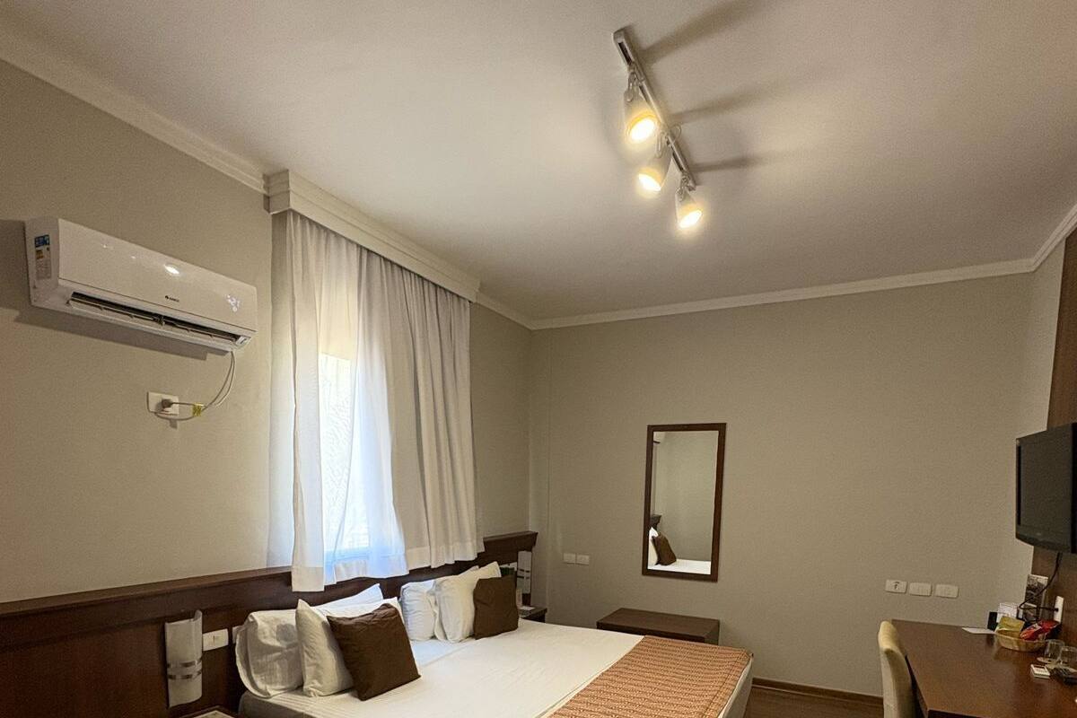 A hotel room with a bed, bedside table, chair, desk, and a television.