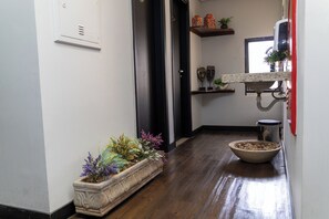 A hallway with a wooden floor, a potted plant, a bowl of pebbles, and a shelf with decorative items. - Class Hotel Passos (Passos)