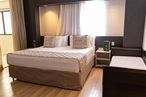 A hotel room with a large bed, a bedside table, a chair, and a window with curtains.