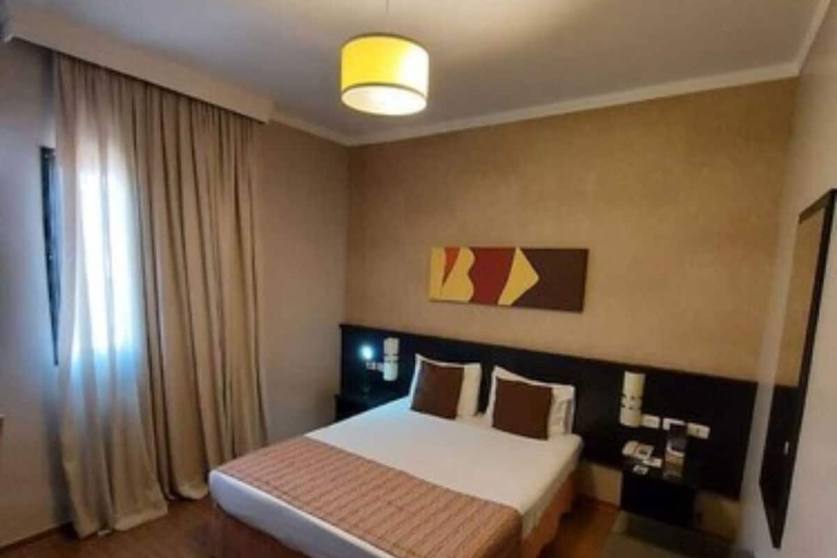 A hotel room with a bed, a nightstand, a lamp, and a painting on the wall.