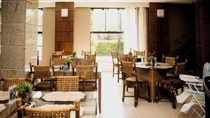 A restaurant with wicker furniture, glass tables, and a view of greenery outside. - Class Hotel Passos (Passos)