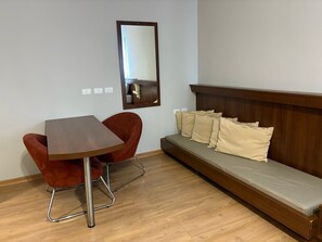 Une pièce avec une table en bois, une chaise rouge, un canapé avec des coussins et un miroir au mur.