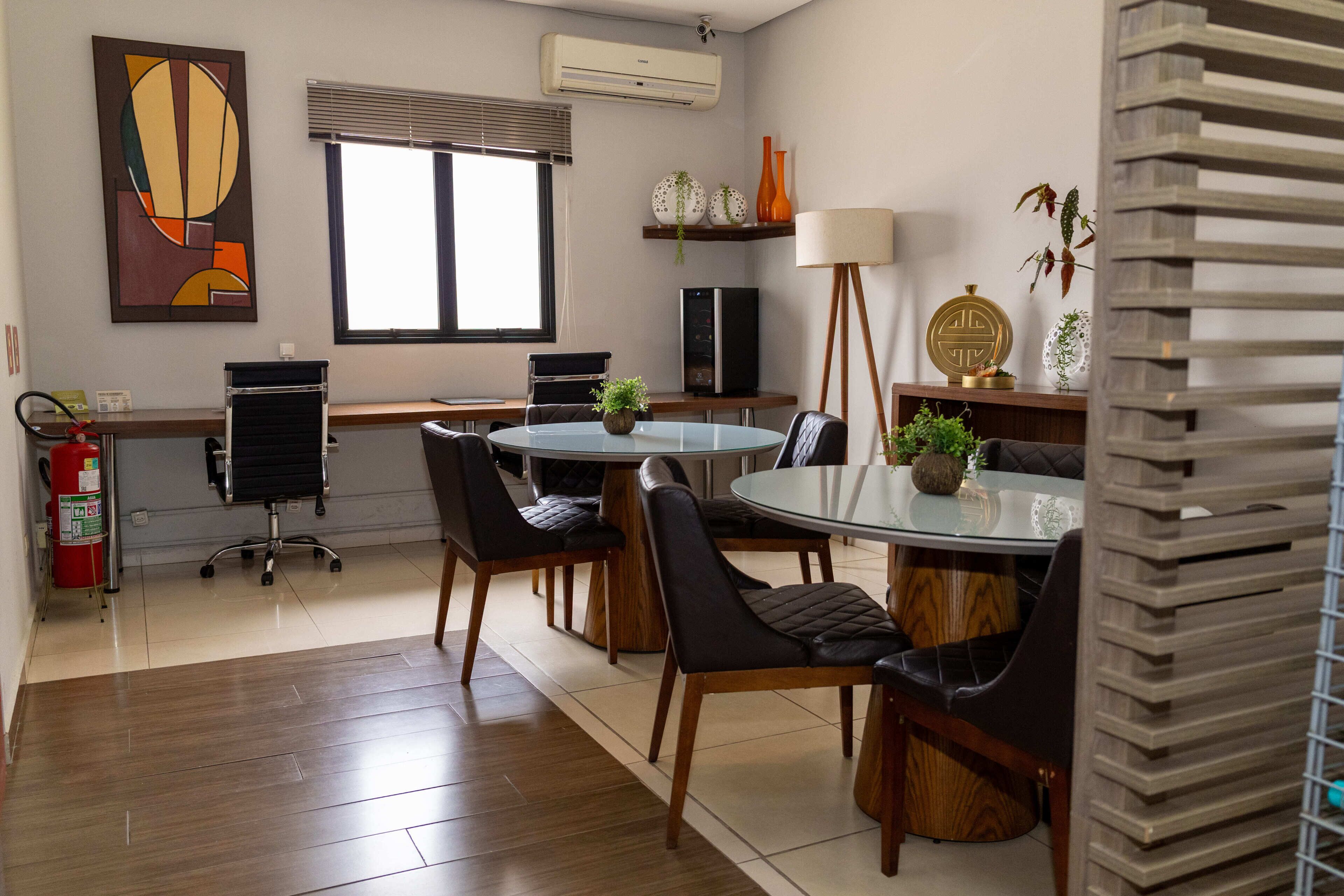Uma sala de reuniões moderna com mesa de vidro, cadeiras de couro, extintor de incêndio e janela com persianas.