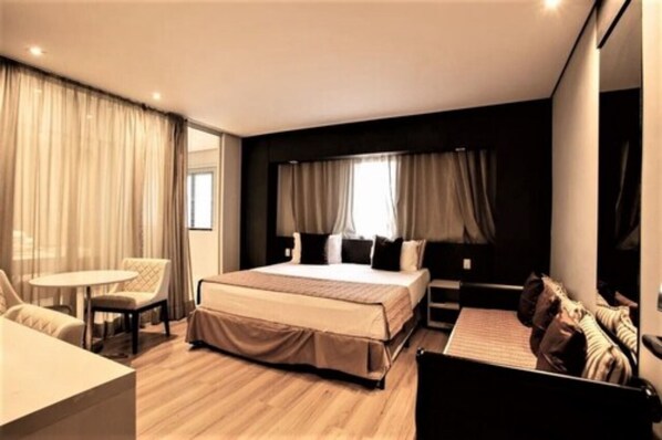 Une chambre d’hôtel moderne dotée d’un grand lit, d’un coin salon avec une table et offrant une vue sur la ville.
