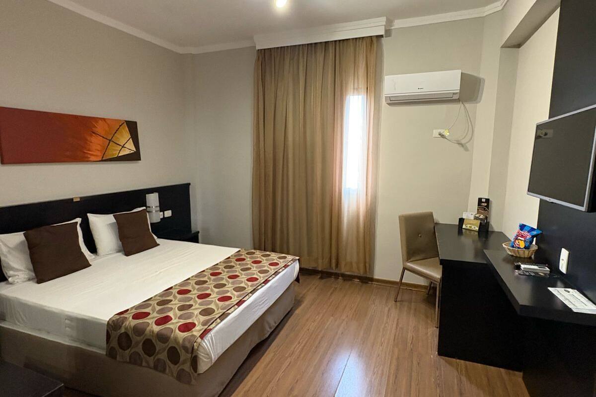 A hotel room with a bed, a desk, a chair, and a TV.