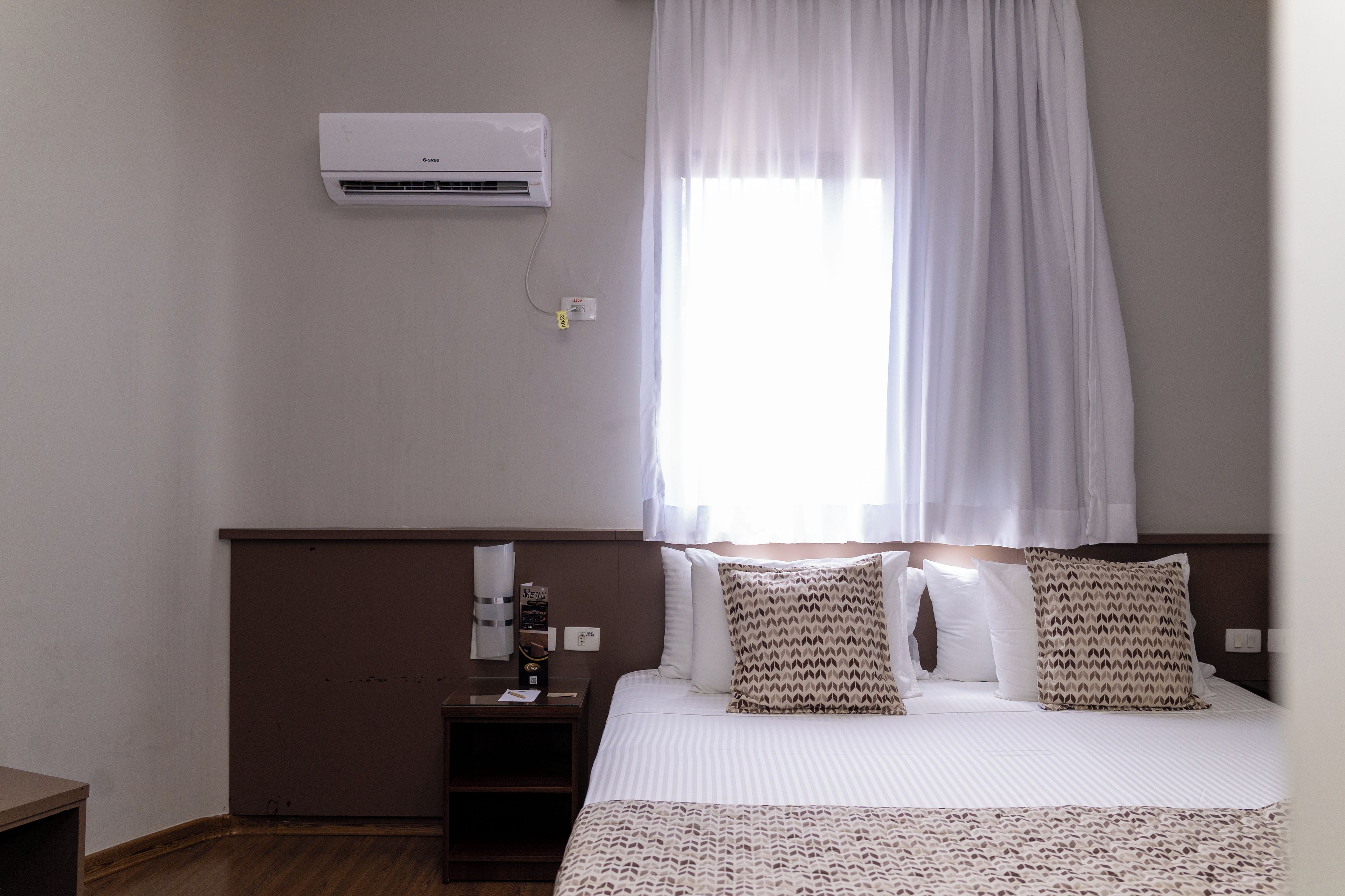Ein Hotelzimmer mit einem Bett, einem Nachttisch, einer Klimaanlage und einem Fenster mit Vorhängen.