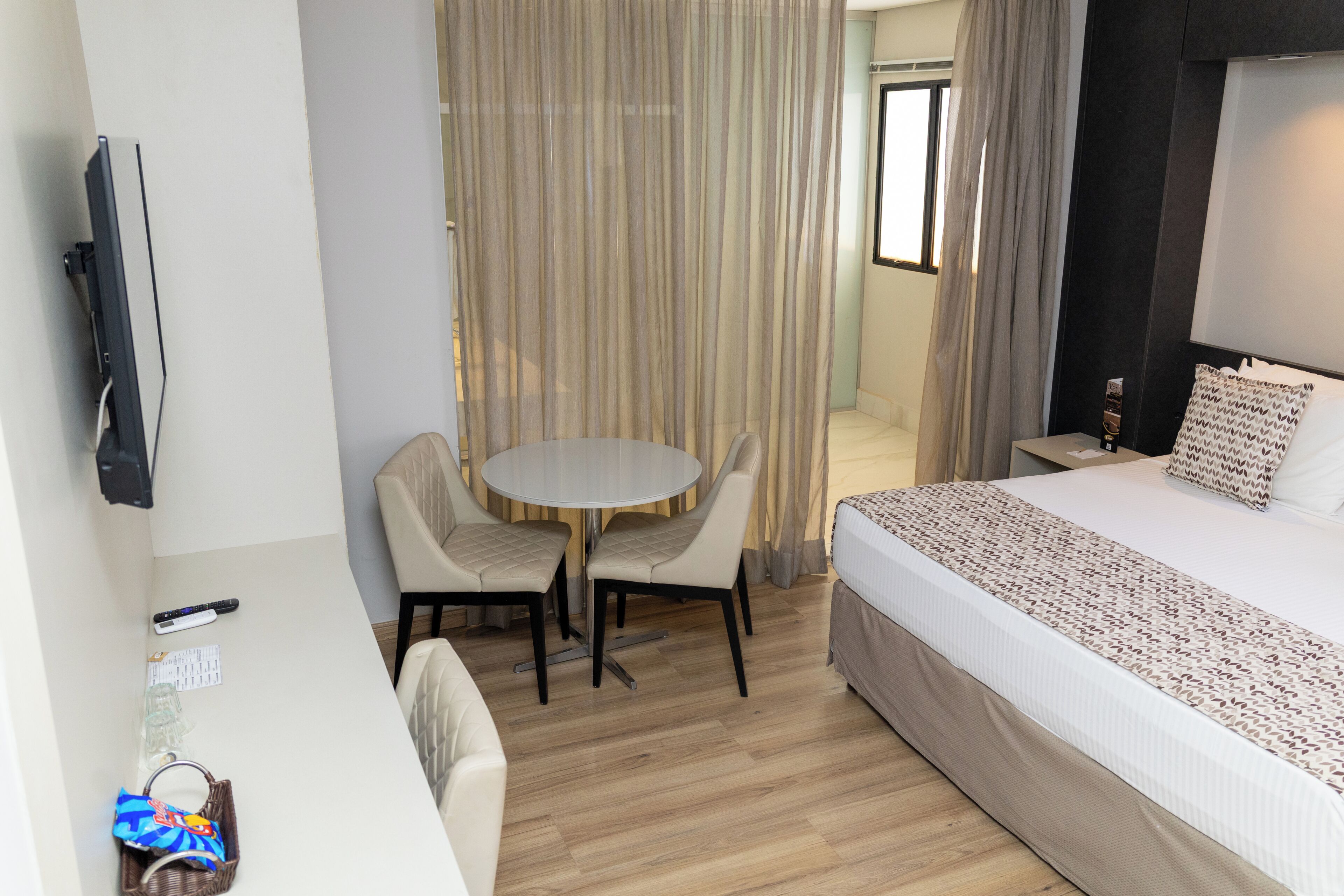 A hotel room with a bed, a desk, a chair, a small table, and a TV.