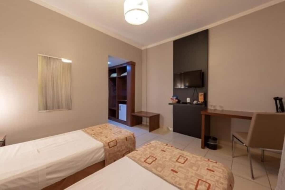 A hotel room with two single beds, a desk, a chair, a television, and a small table.