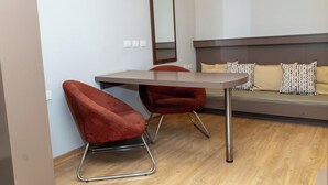 A modern room with a wooden floor, a grey sofa with patterned cushions, and two red upholstered chairs with metal legs. - Class Hotel Passos (Passos)