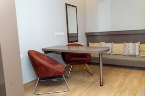 A modern room with a wooden floor, a grey sofa with patterned cushions, and two red upholstered chairs with metal legs. - Class Hotel Passos (Passos)