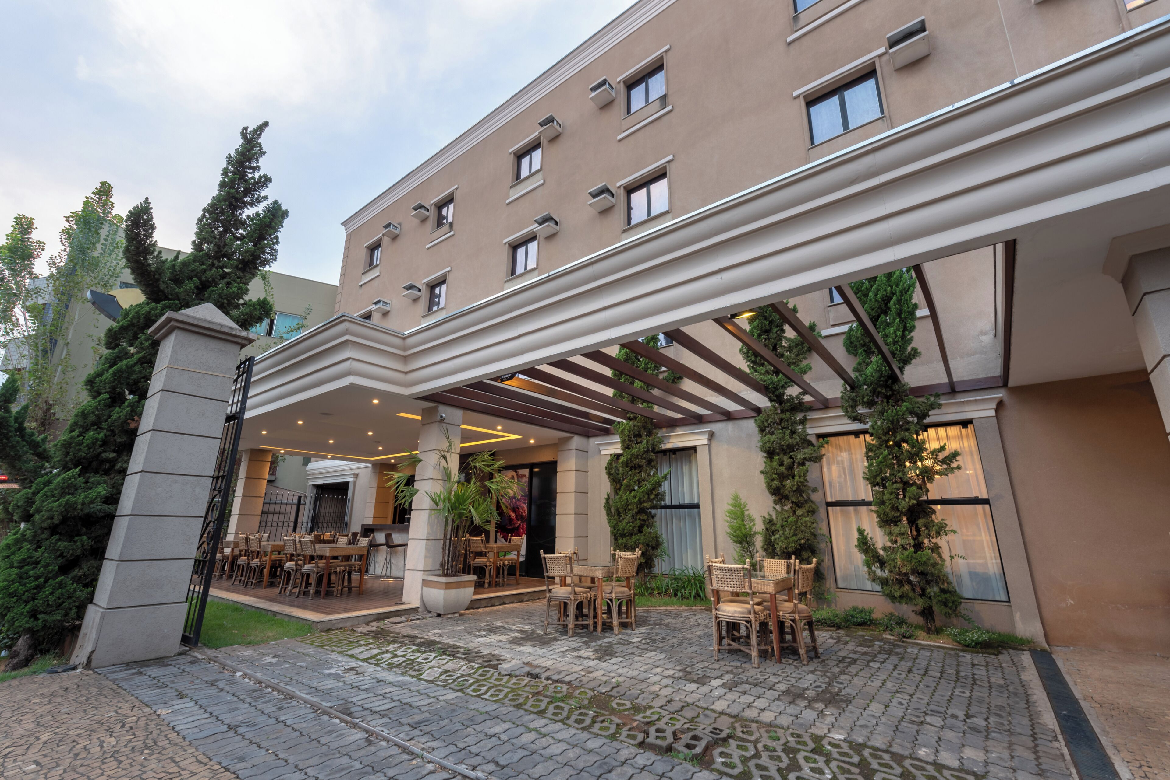 A hotel entrance with a covered patio area, outdoor seating, and a stone-paved walkway.