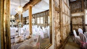 A rustic venue with high ceilings and exposed brick walls, featuring tables set for a formal event.