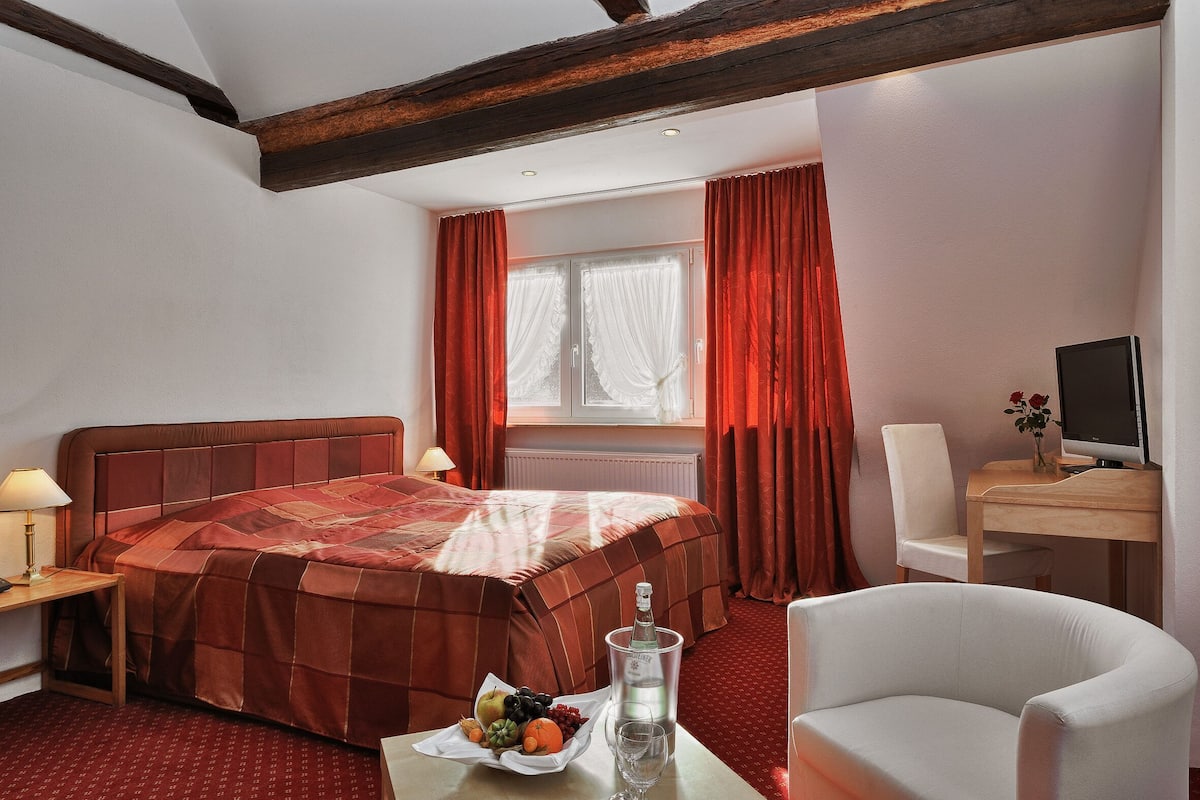 Een hotelkamer met een bed, bureau, stoel, televisie en een raam met gordijnen.