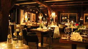 A restaurant with wooden beams, chandeliers, and tables set for dining.