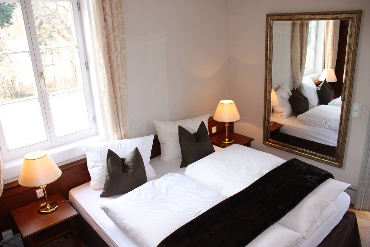 Een hotelkamer met een bed, twee bedlampen, een grote spiegel en een raam met gordijnen.