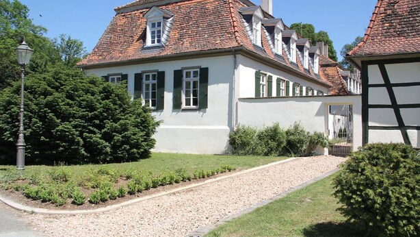 A traditional European-style building with a symmetrical facade, multiple chimneys, and a gravel driveway leading to the entrance.