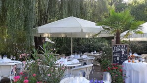 An outdoor dining area with round tables, white tablecloths, and wicker chairs.