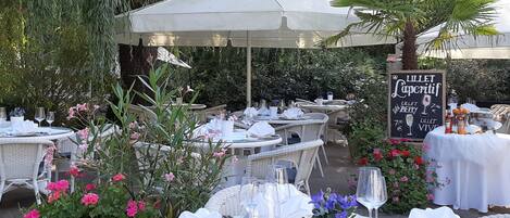 An outdoor dining area with round tables, white tablecloths, and wicker chairs.