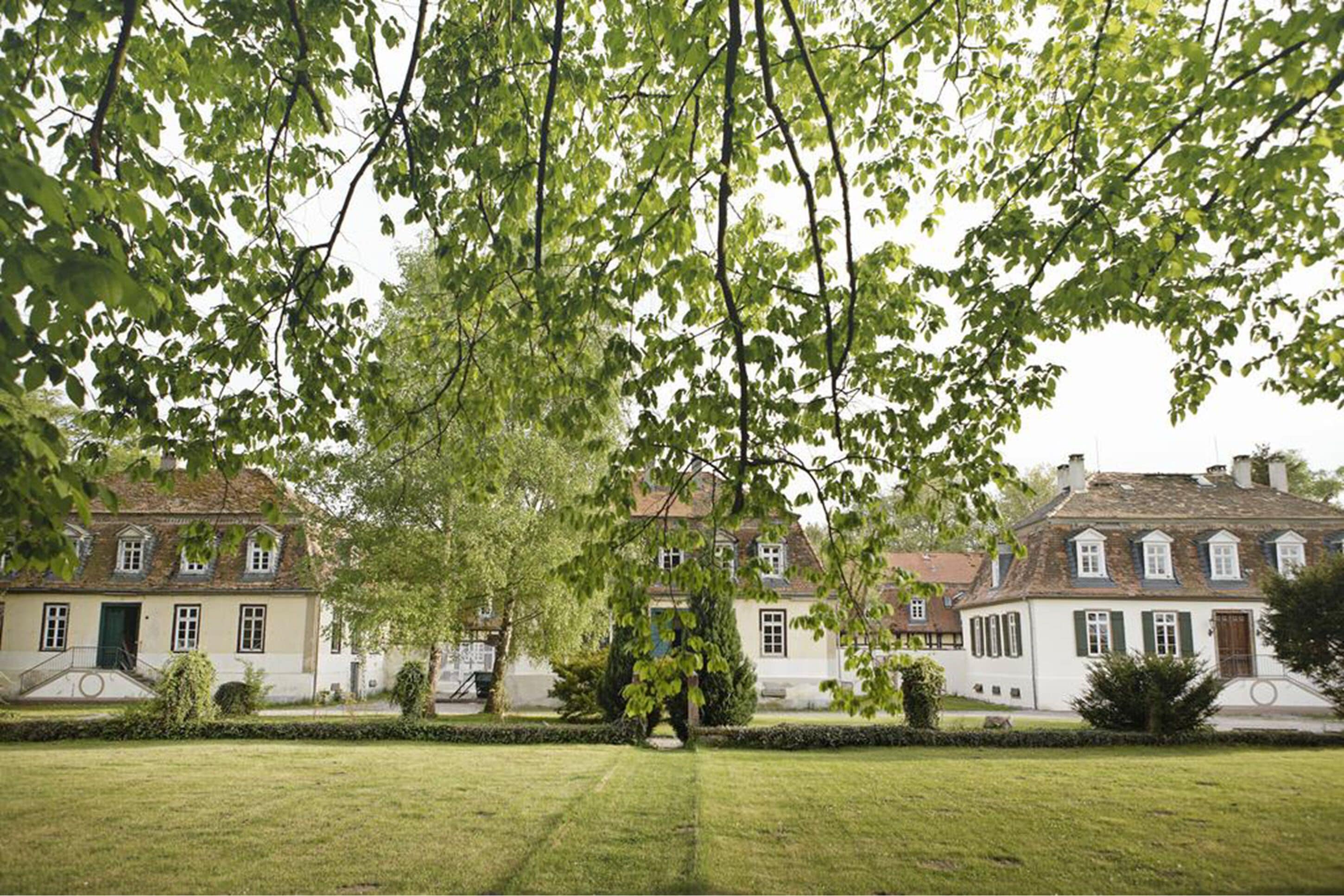 Edifici d'estil europeu tradicional amb arquitectura simètrica, gespa ben cuidada i arbres madurs que ofereixen ombra.