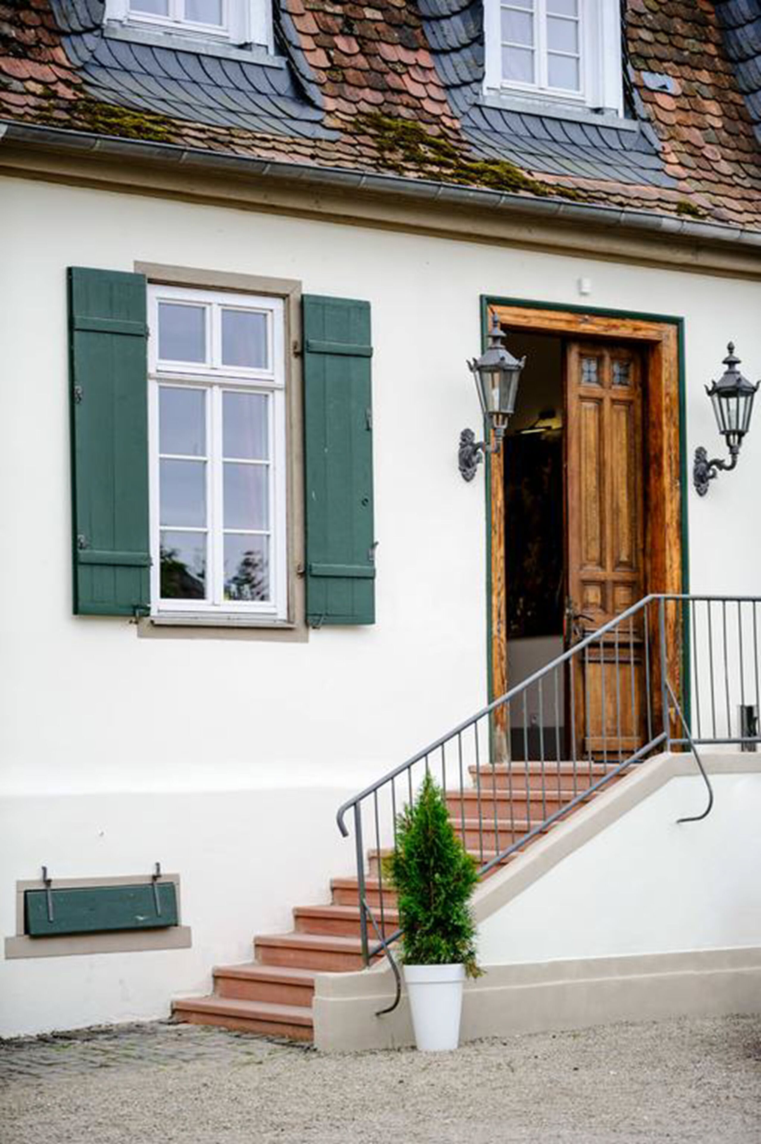 A building with a white exterior, green shutters, a wooden door, and a small staircase leading to the entrance.