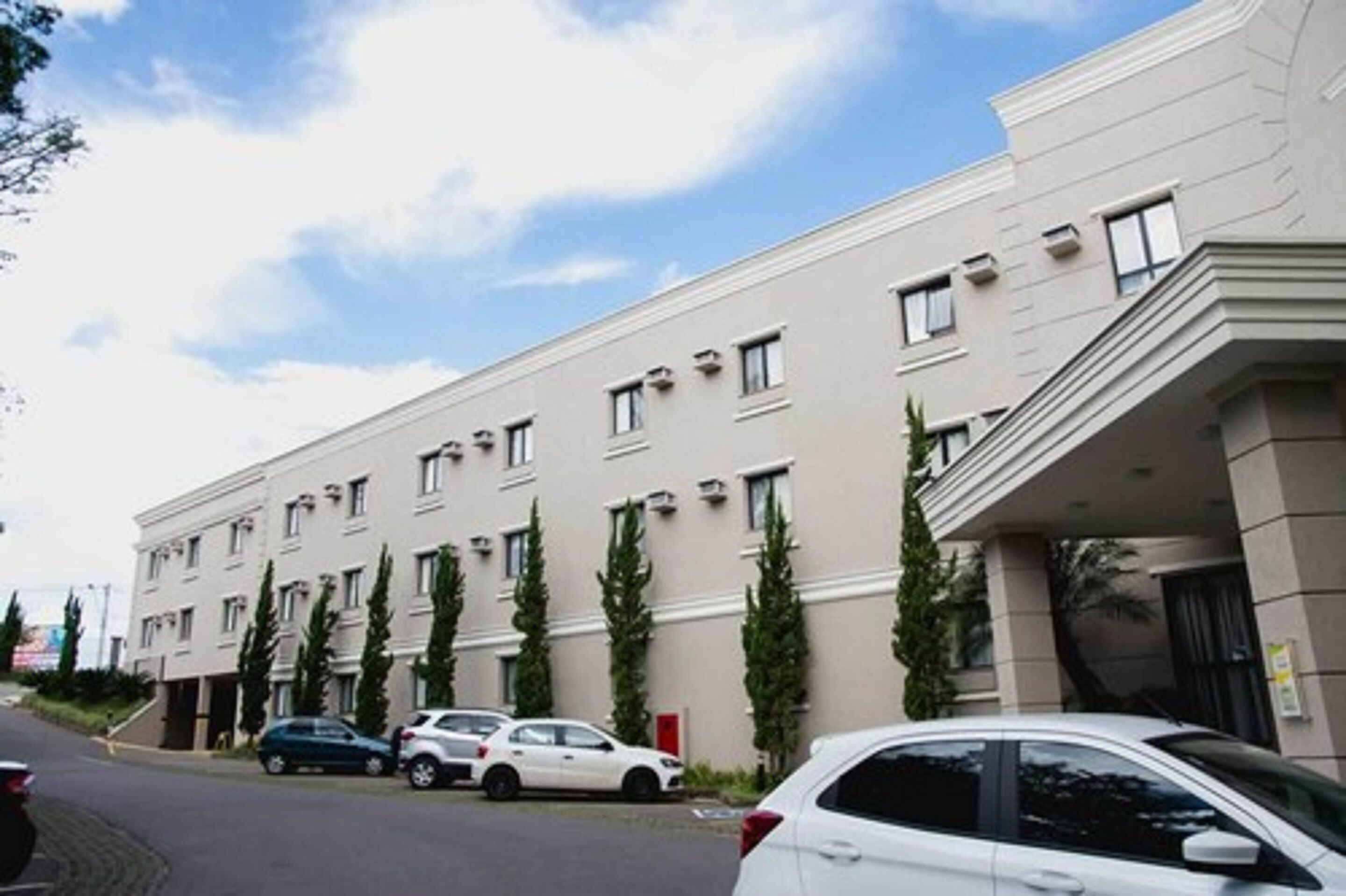Un immeuble à plusieurs étages doté d’une façade plate, de nombreuses fenêtres et d’un espace de stationnement où sont garées des voitures.