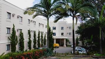 A multi-story hotel with a symmetrical facade, palm trees, and a parking area.