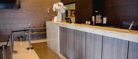 A reception area with a marble counter, a TV mounted on the wall, and a vase with white flowers.