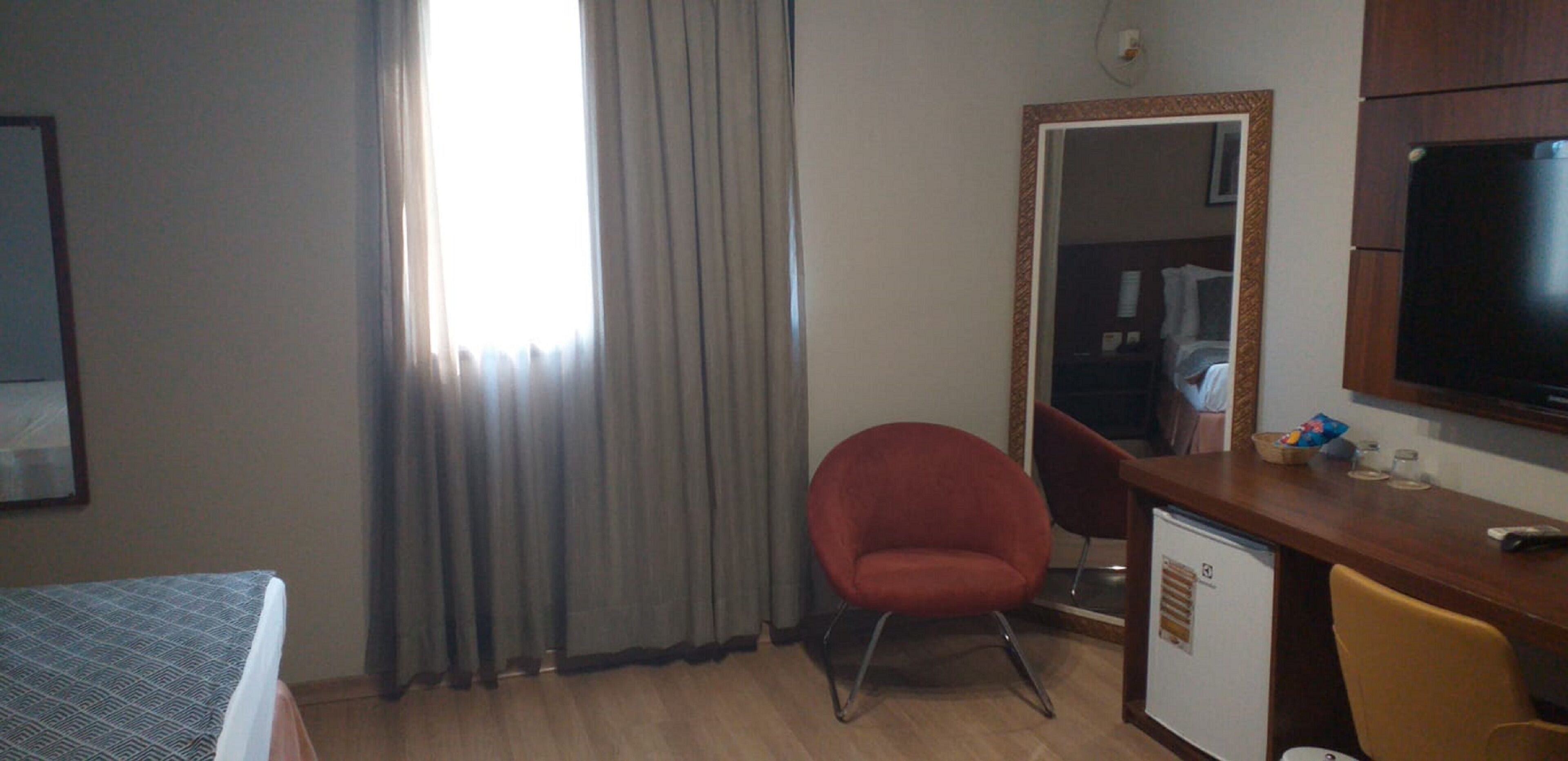 Une chambre d’hôtel équipée d’un lit, d’un bureau, d’une chaise, d’une télévision et d’une fenêtre avec des rideaux.
