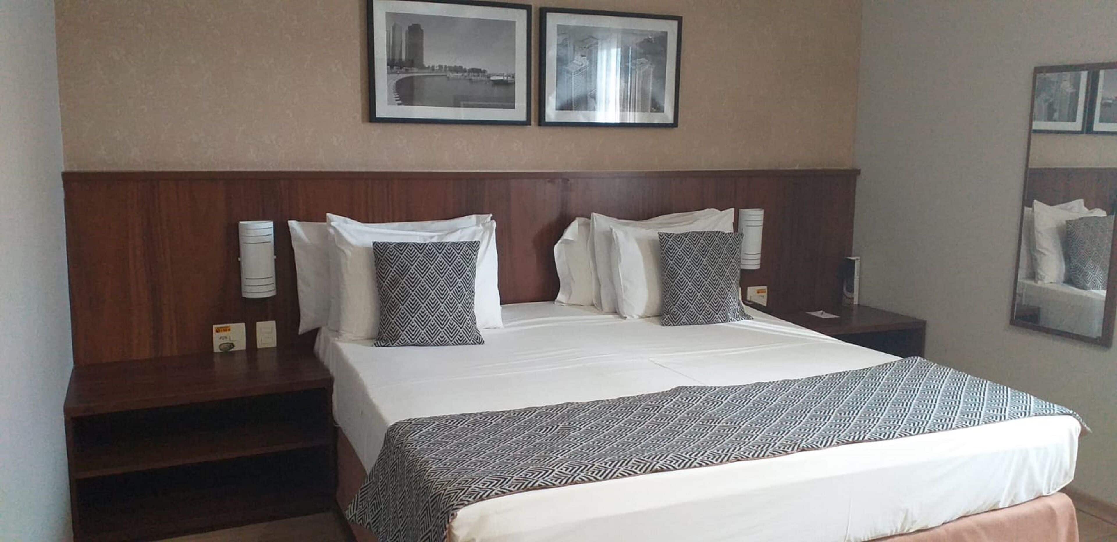 A hotel room with a large bed, two bedside tables, and two framed pictures on the wall.