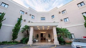 A hotel with a symmetrical facade, multiple windows, and a central entrance with a covered walkway. - Class Hotel Varginha (Varginha)