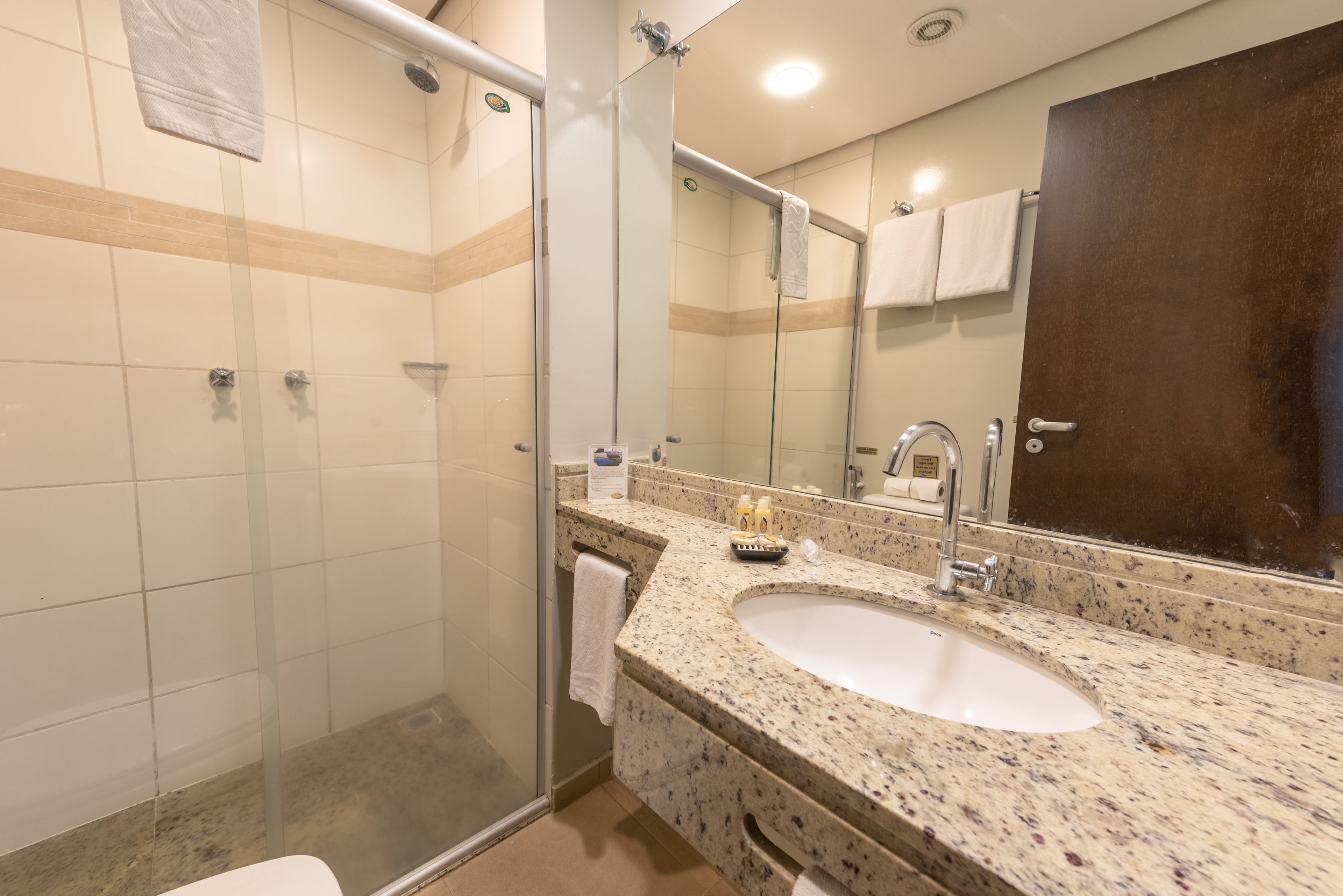 A bathroom with a glass-enclosed shower, a sink with a mirror, and a towel hanging on the wall.