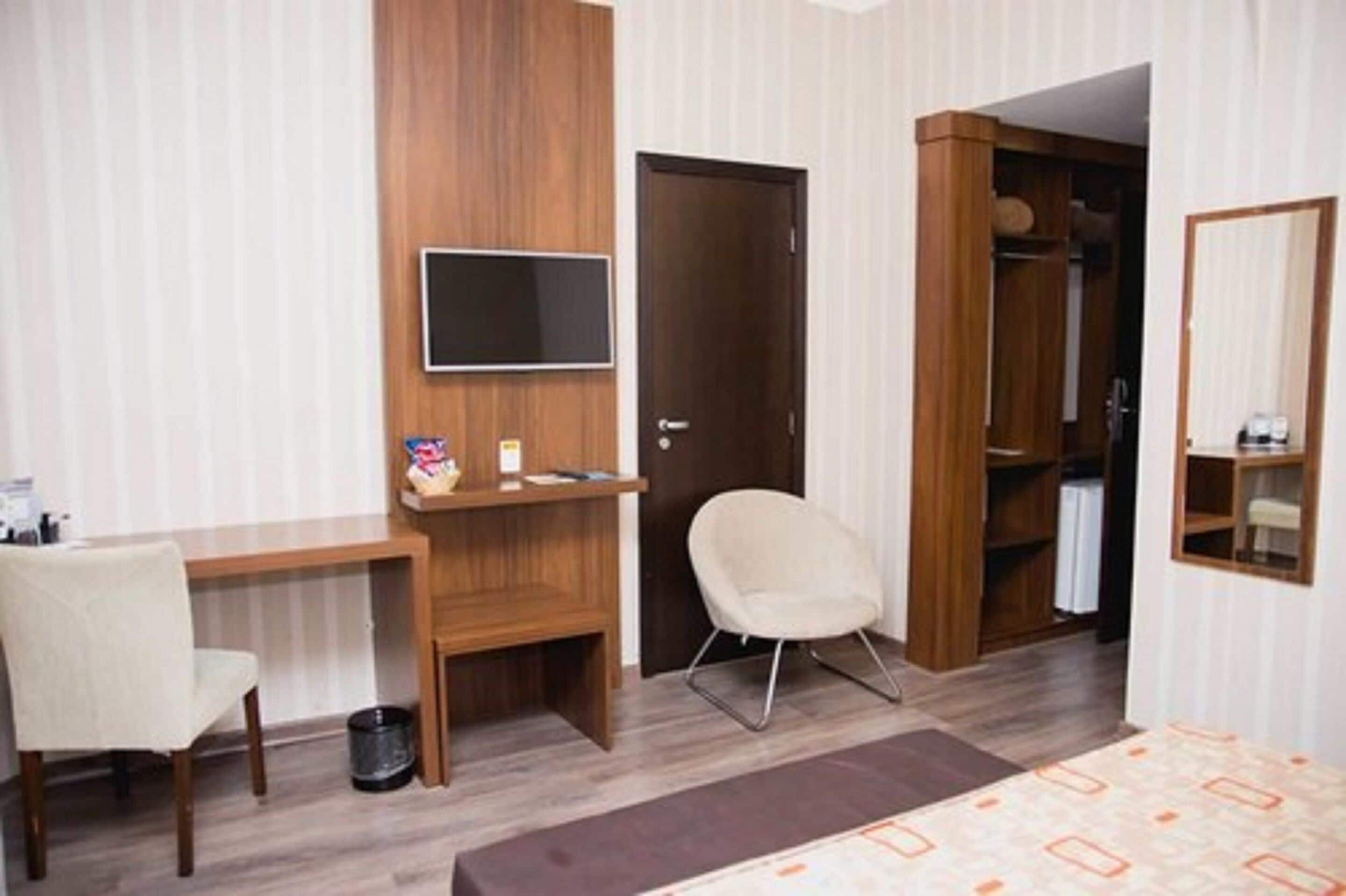 Habitación de hotel con escritorio de madera, una silla, televisor, armario y cama.