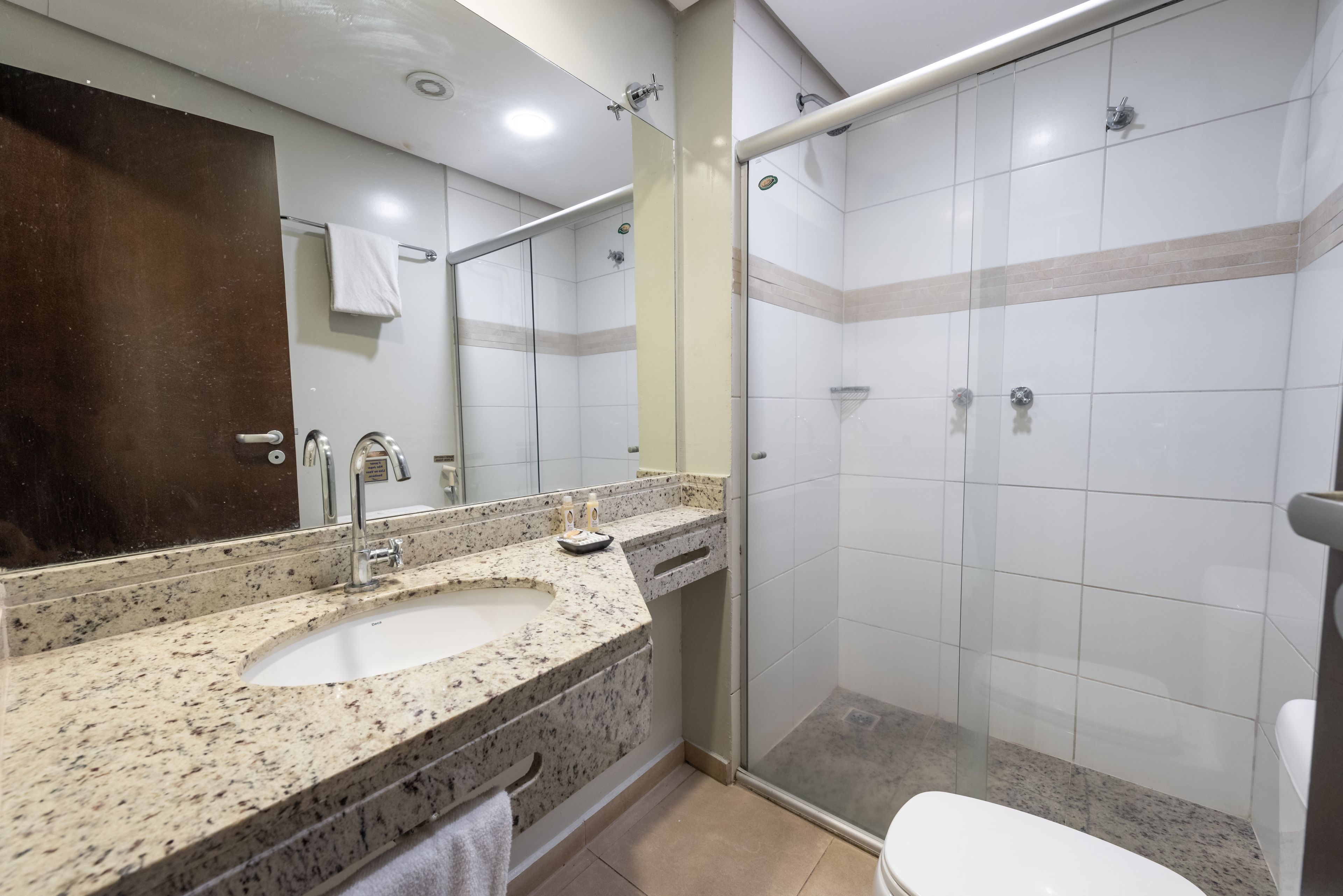 Et badeværelse med vask i granit, et spejl, en glas brusekabine og et toilet.
