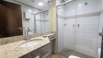 Et badeværelse med vask i granit, et spejl, en glas brusekabine og et toilet.