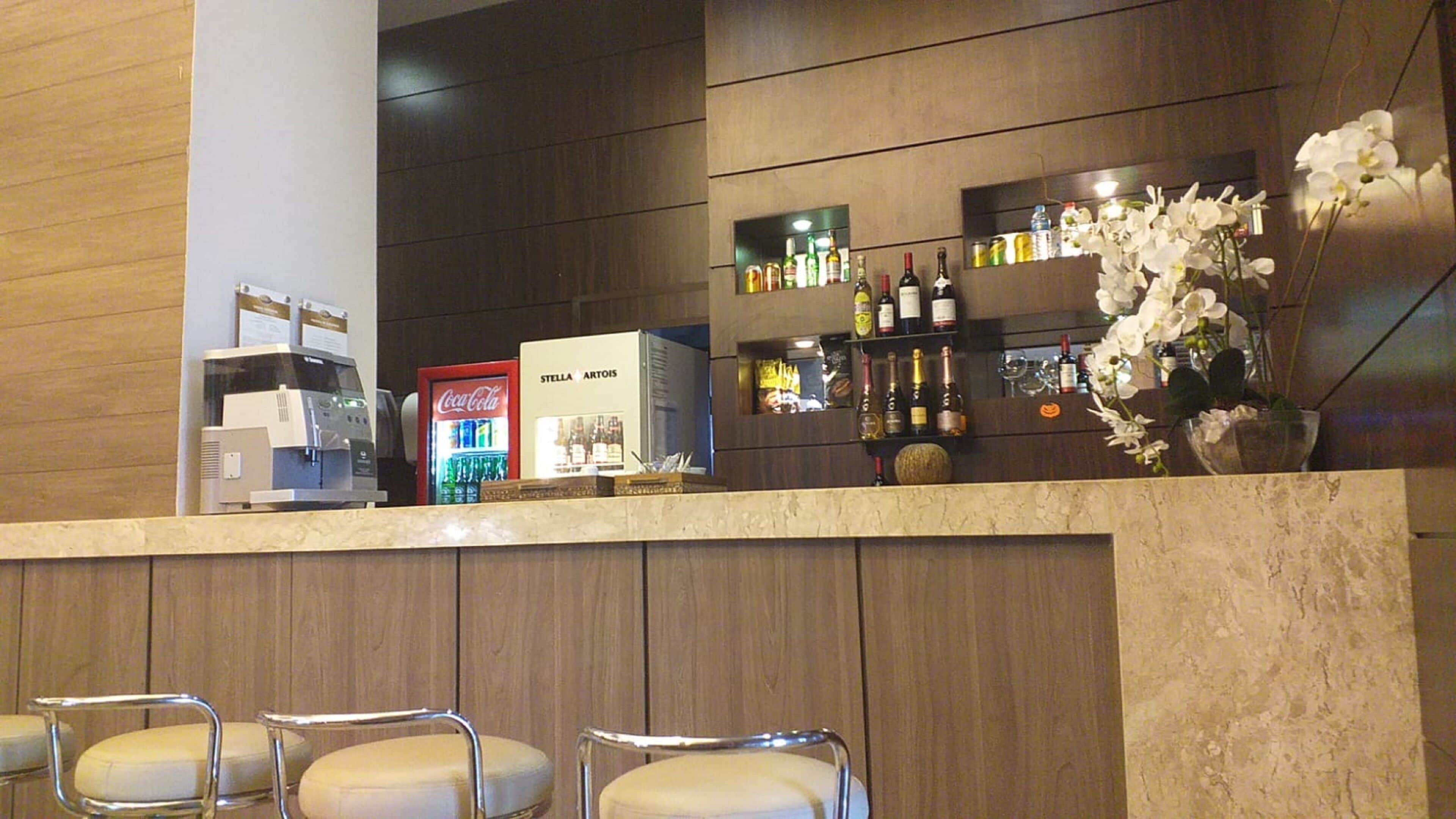 Angolo bar con posti a sedere, un frigorifero Coca-Cola e diverse bottiglie sugli scaffali.