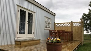 A white building with a wooden deck and a large planter with flowers. - Gamla húsið - The old house (Sveitarfélagid Ölfus)