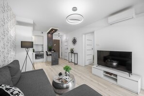 A modern living room with a flat-screen TV, grey sofa, and a coffee table with magazines and a plant. - Emihouse Cityvibe Apartments Rzeszów (Rzeszów)