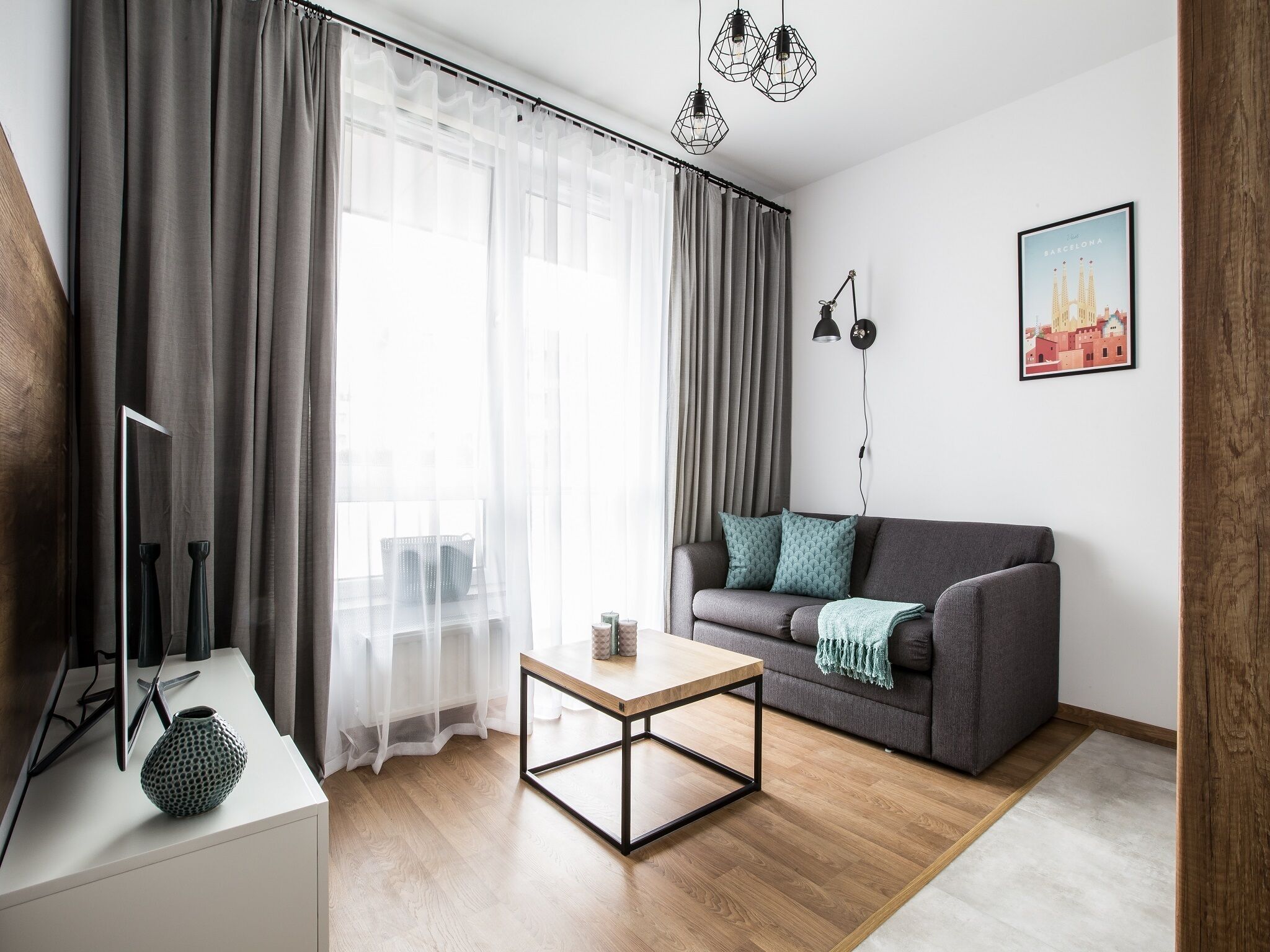 A modern living room with a grey sofa, a wooden coffee table, and a large window with sheer curtains.