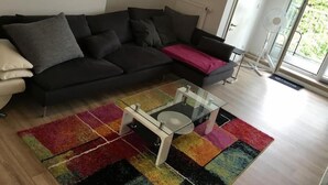 Ein modernes Wohnzimmer mit einem schwarzen Sofa, einem Glastisch und einem farbenfrohen Teppich.